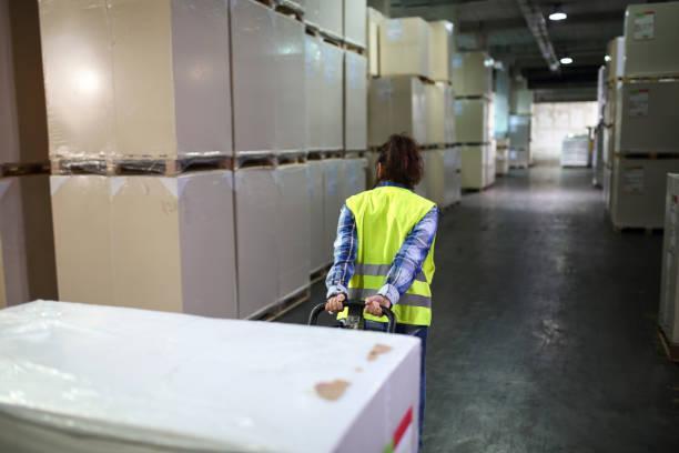 Female worker transporting boxes in warehouse Female worker transporting boxes in warehouse. Woman is pulling hand truck at workplace, Optimizing Supply Chains: The Role Of Cold Storage Services stock pictures, royalty-free photos & images