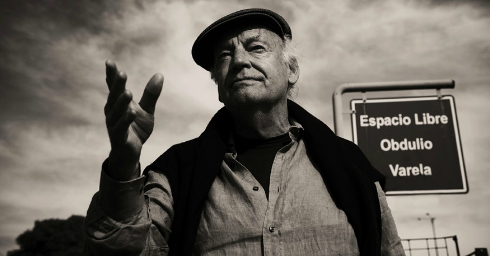 In this sepia toned image, writer and activist Eduardo Galeano looks past the camera and reaches out his right hand in front of him.