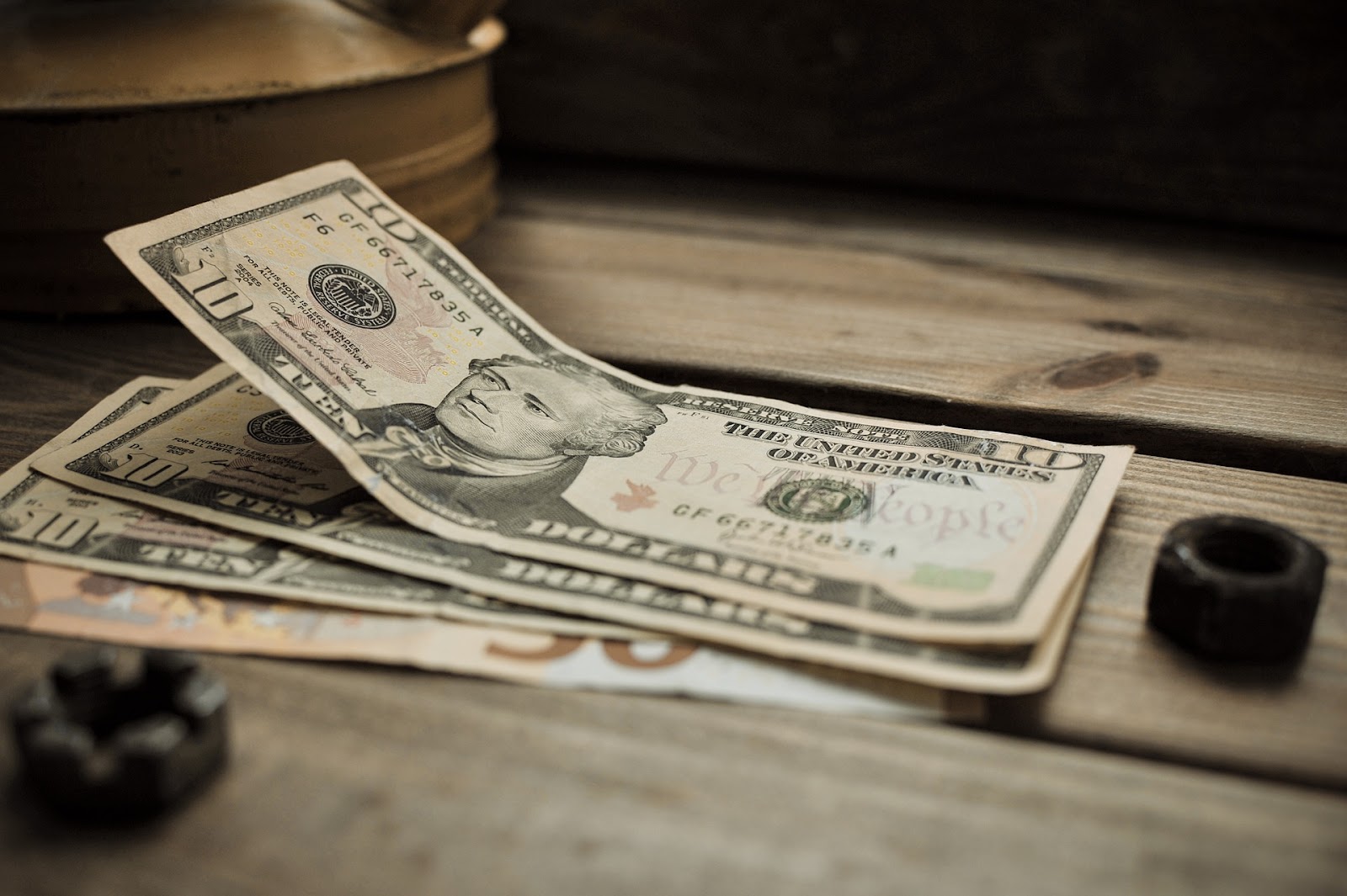 An image of three $10 bills on a slatted wooden table.