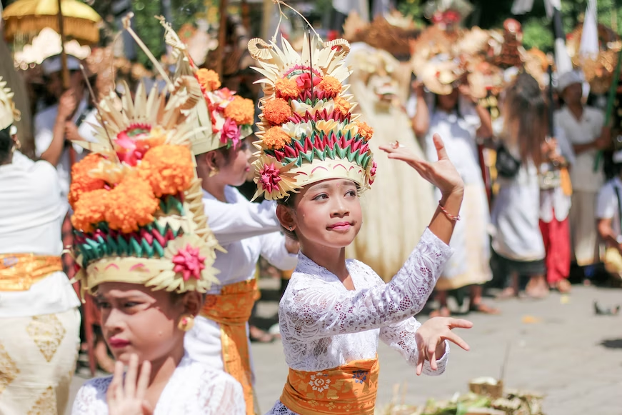 Young woman in a white lace dress adorned with a vibrant yellow and red flower headdress, participating in a traditional Balinese ceremony or ritual.