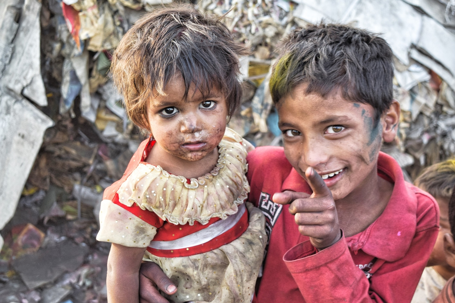 Two young children in dirty and tattered clothes smiling at the camera.