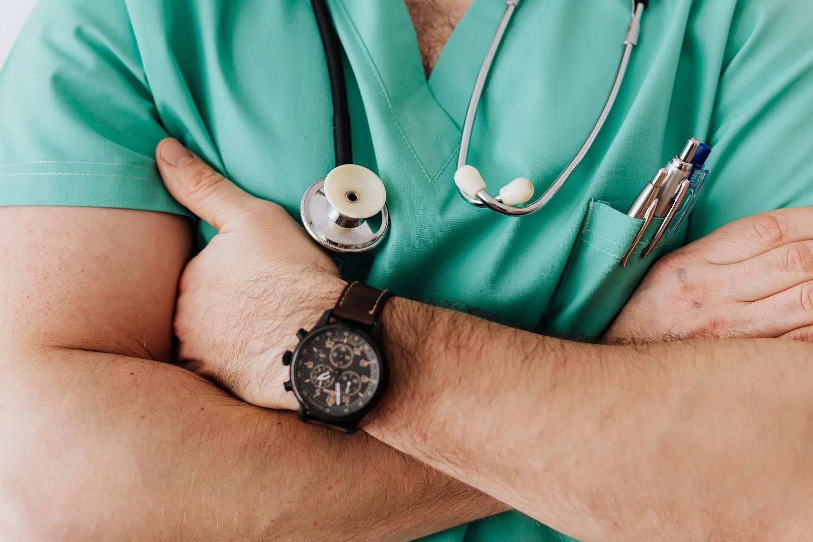 A man wearing a green doctor robe and a stethoscope, showing his hands folded across his chest