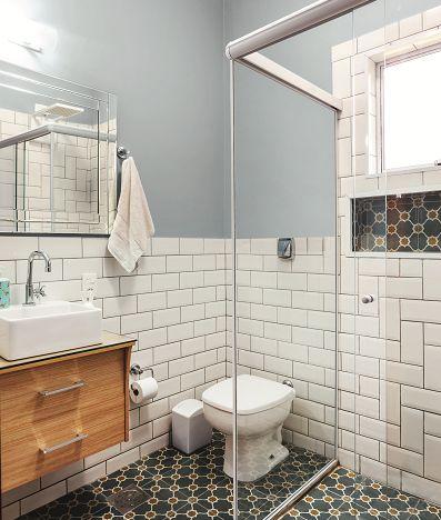 Banheiro com meia parede inferior com azulejo subway branco e outra metade pintada de azul, piso ladrilho hidráulico azul, box de vidro e armário de madeira.