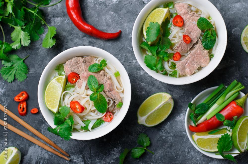 Traditional Vietnamese Soup Pho Bo with Rice Noodles, Beef and Herbs on Dark Background