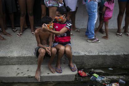 Una niña ayuda a un niño a ponerse una mascarilla mientras los residentes hacen fila para recibir bolsas de alimentos gratis en el barrio de Vila Vintem, en Río de Janeiro, Brasil.
