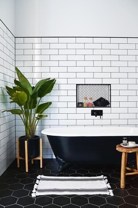 banheiro em estilo retrô com azulejo subway tiles branco nas paredes, piso ladrilho hidráulico ´preto, banheira preta e branca, vasos de plantas e detalhes do banheiro preto.