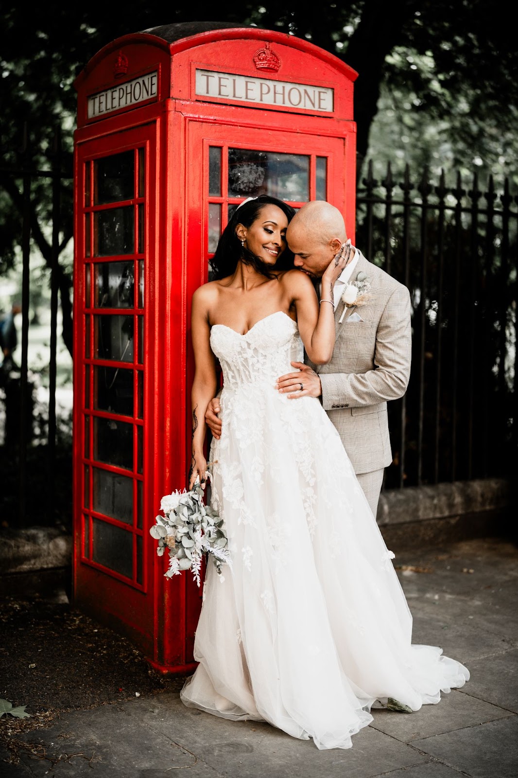 Bride and groom holding eachother in front of a red London phonebooth