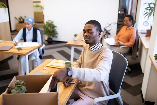 homem jovem negro se prepara para começar o trabalho em um escritório, ao fundo vemos mais duas pessoas também sentadas em suas mesas