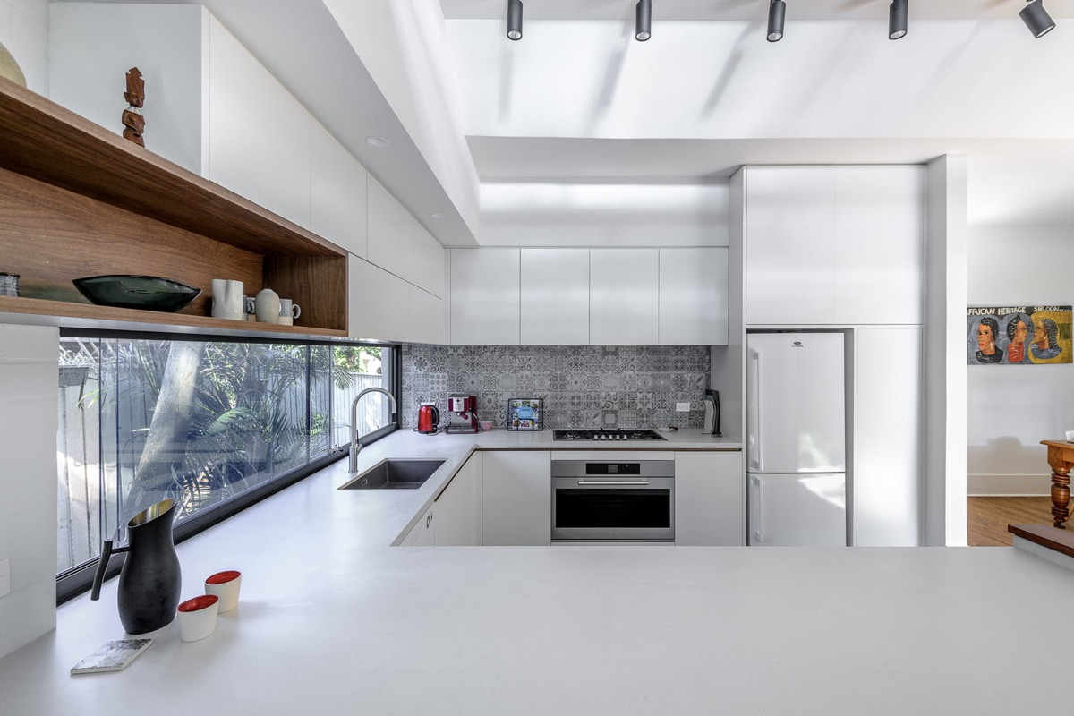 natural lit modern u-shaped kitchen featuring white flat panel cabinets, large horizontal window above the sink and a patterned tile backsplash