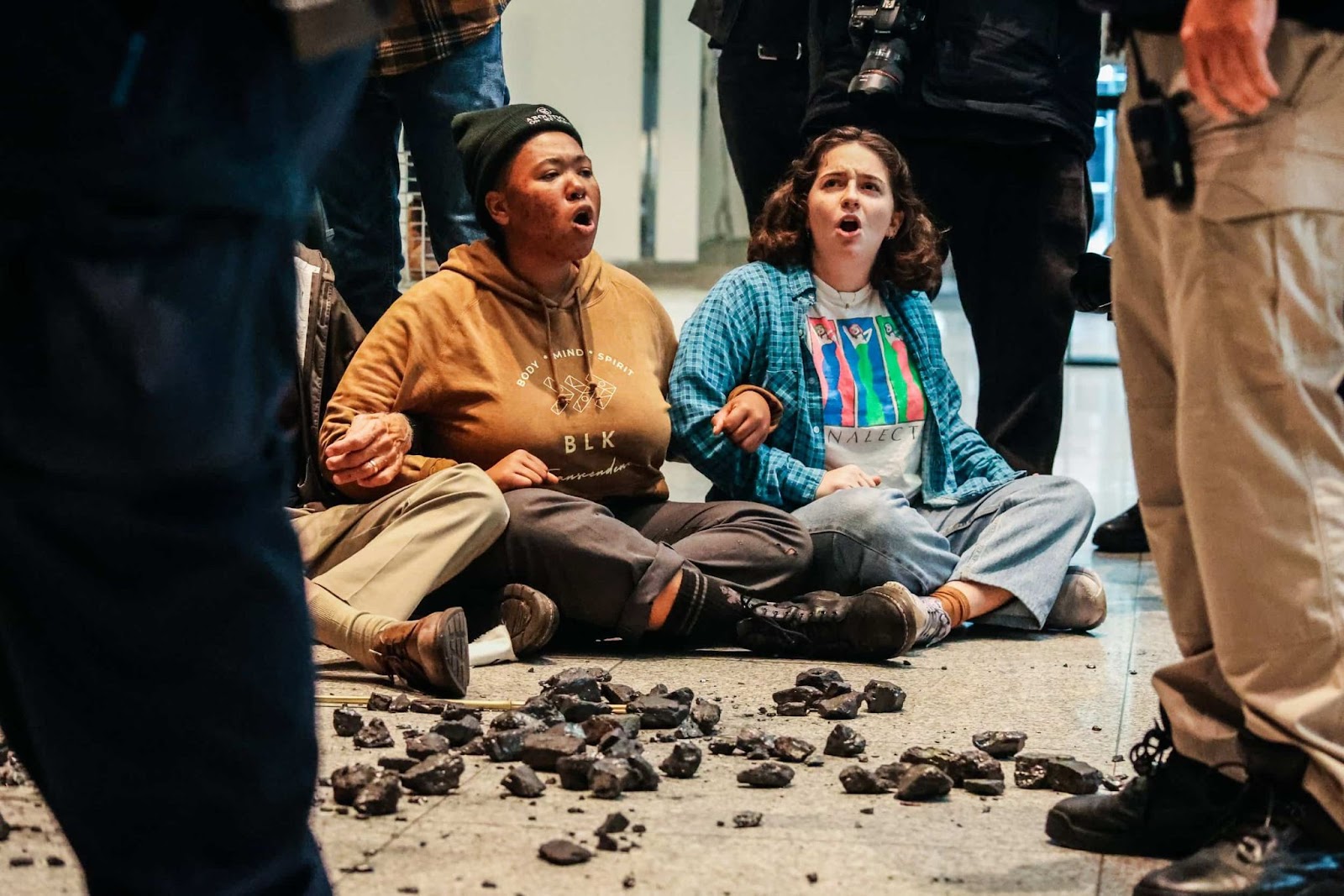 rebels kneel and chant among rocks of coal spread over a polished stone floor of a foyer