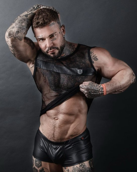 Danny Star posing in black leather fetish shorts and black mesh shirts lifting it over his abs to reveal his muscles