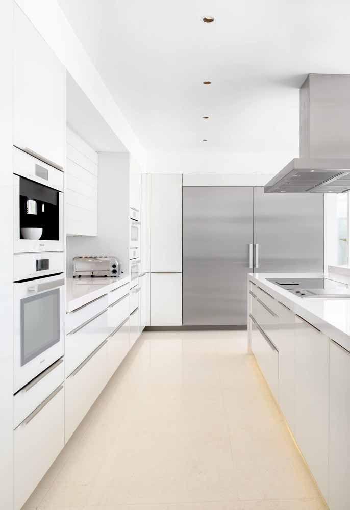 Cozinha grande com armários brancos, piso em tom neutro e eletrodomésticos de inox