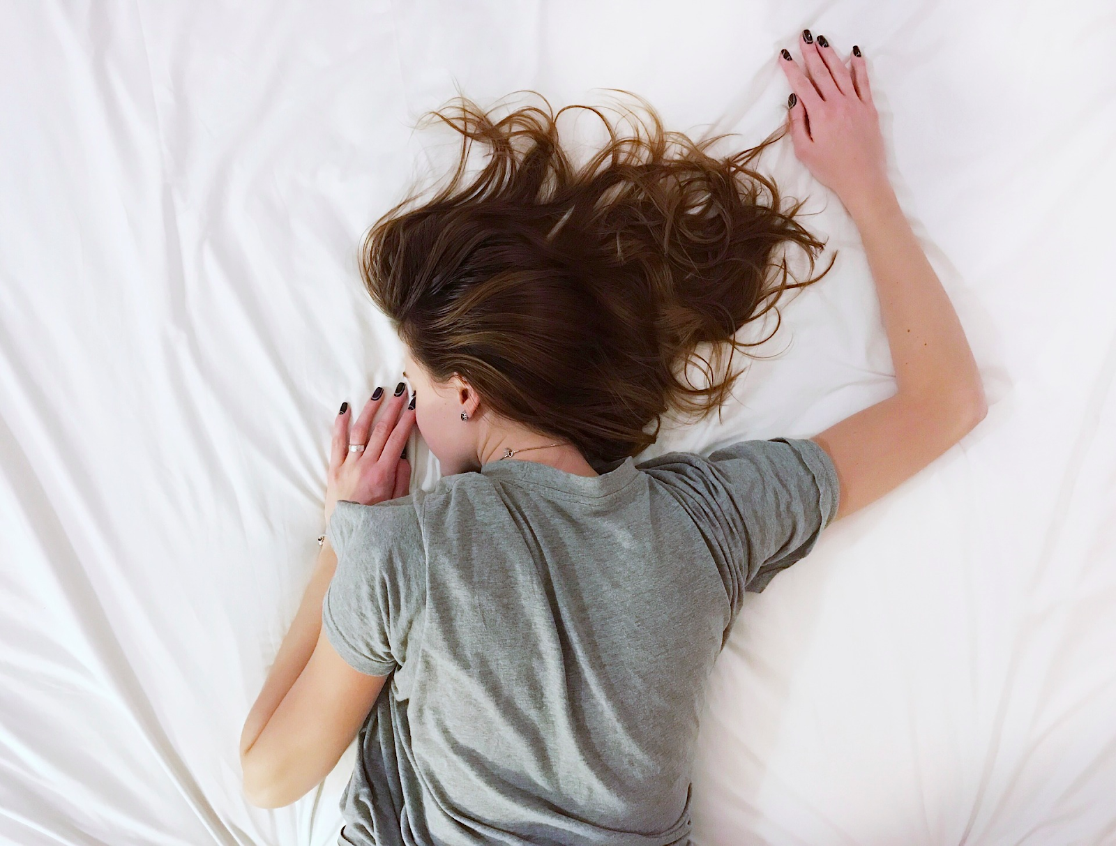 Woman sleeping on her stomach with her hair spread out on white sheets