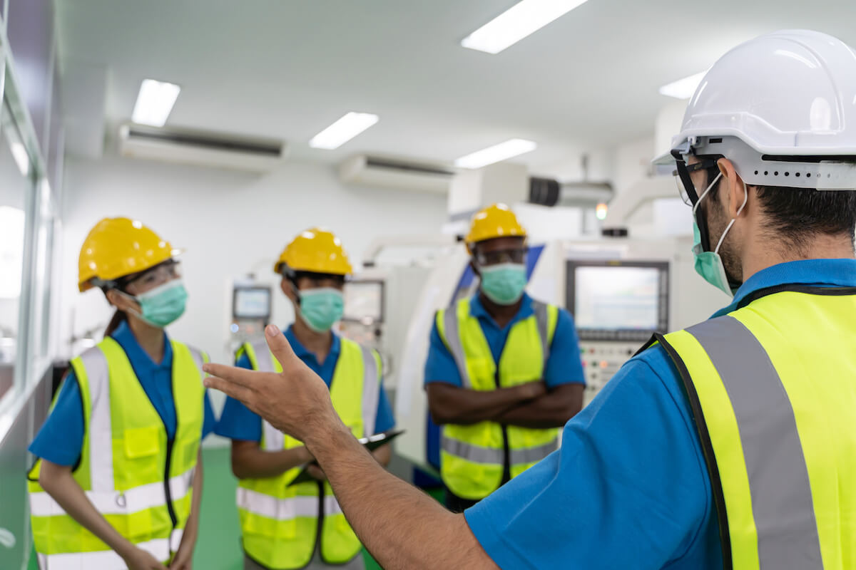 Compliance in risk management: employees wearing hard hats, safety goggles, reflectorized vests, and masks