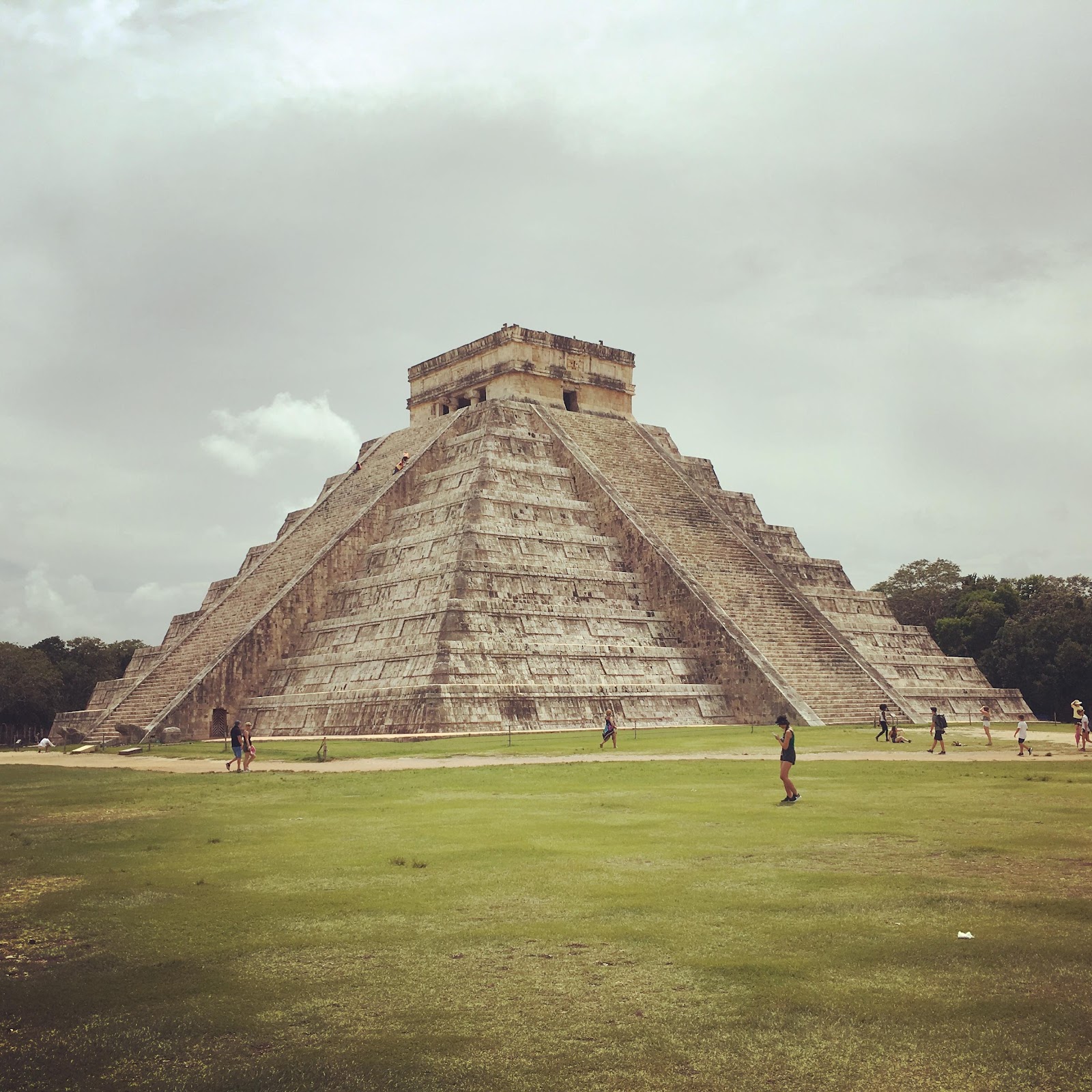 a pyramid in a grassy field with Chichen Itza in the background