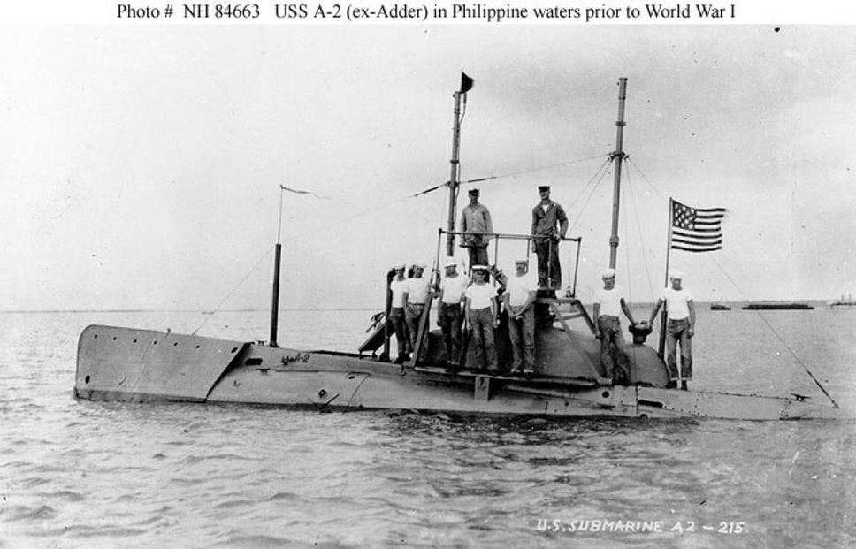 Historical black and white photo of U.S. Navy Soilders wearing white t-shirts while standing on top of a submarine deck in the Philippine waters prior to World War I.