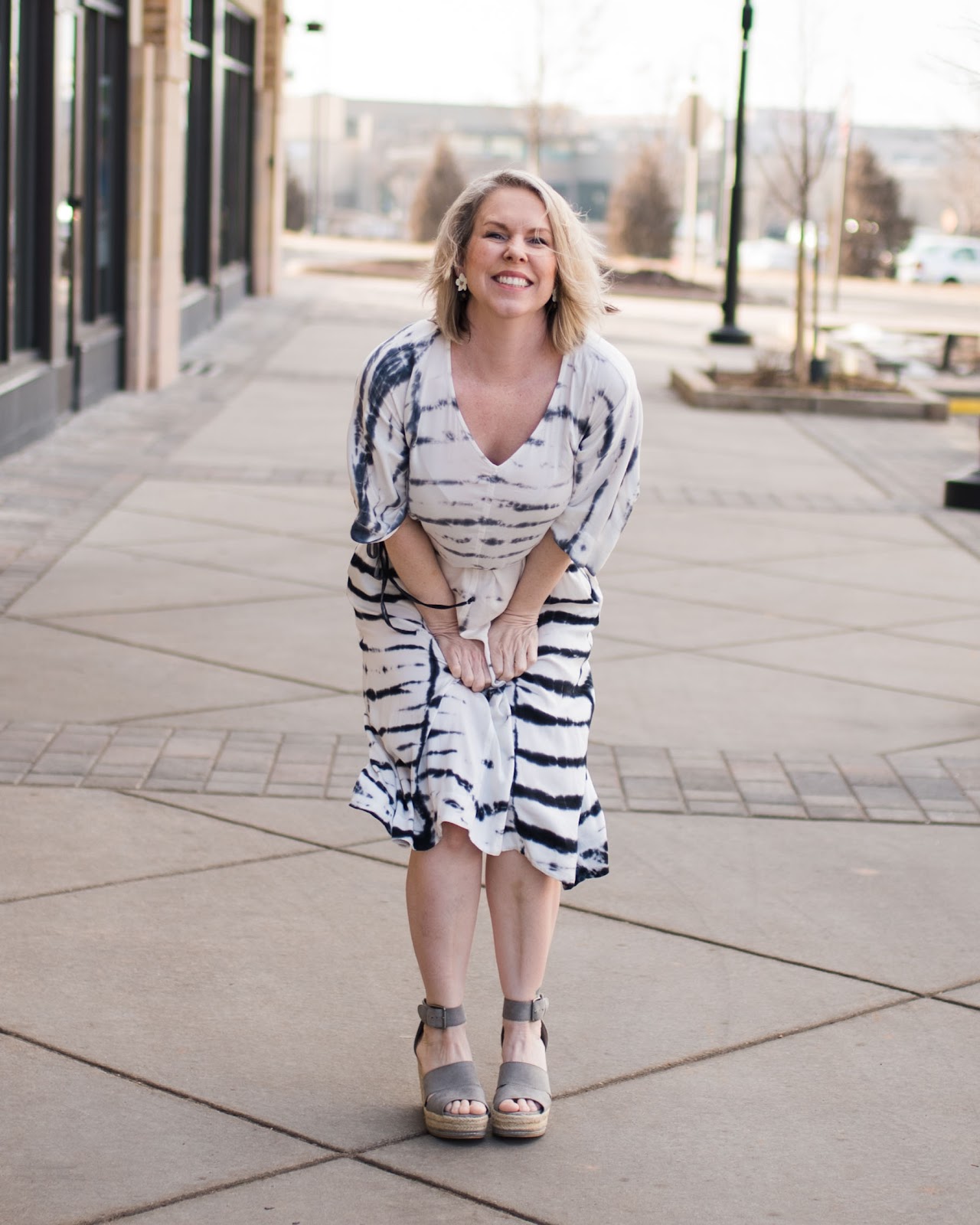 Smiling Amanda in a white striped dress on a city sidewalk.