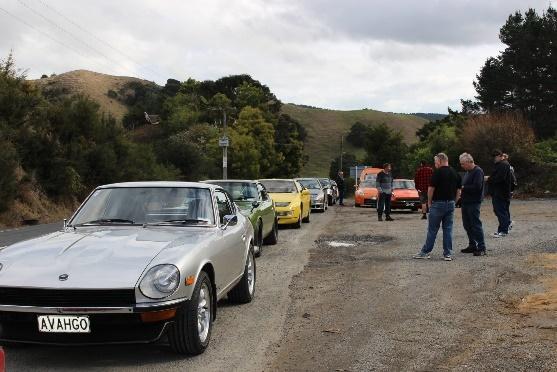 A group of people standing next to cars parked on a dirt road Description automatically generated with medium confidence