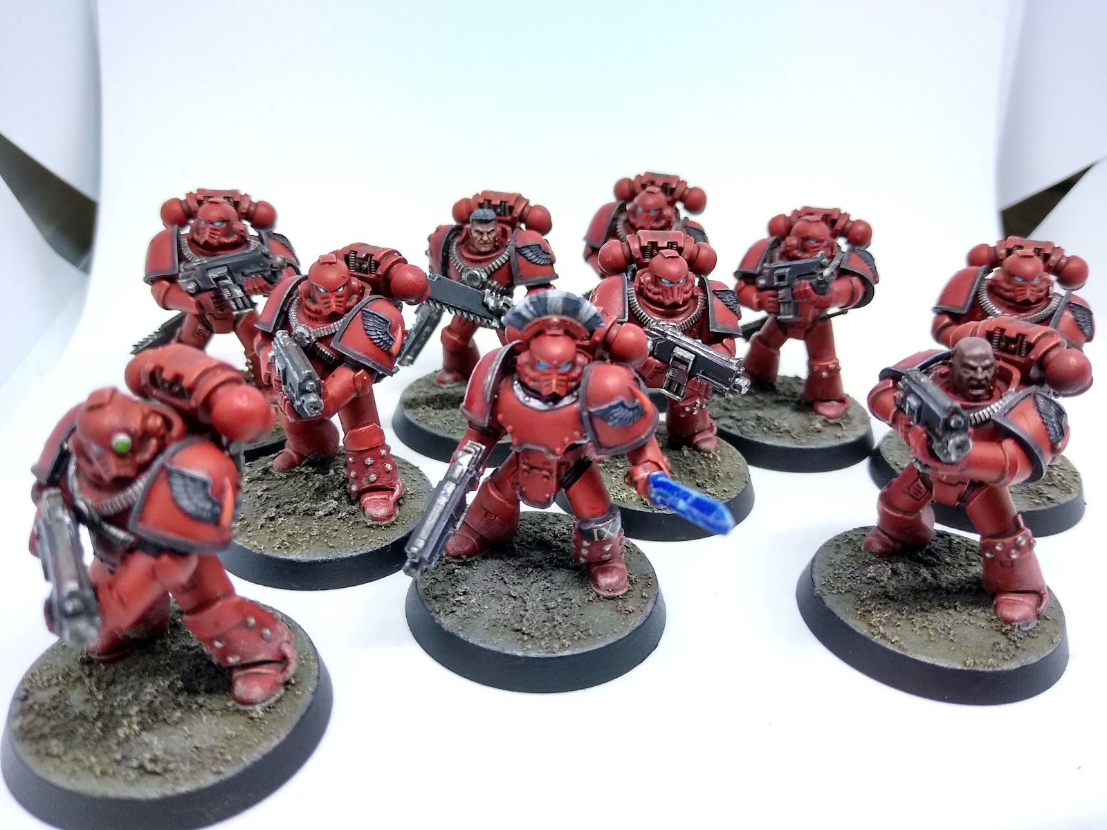 A squad of 10 space marines painted in the legion colours of the Blood Angels, red armour with black trim. They are armed with bolters and combat blades, and the sergeant additionally has a power sword along with a black-and-white crest on his helmet.