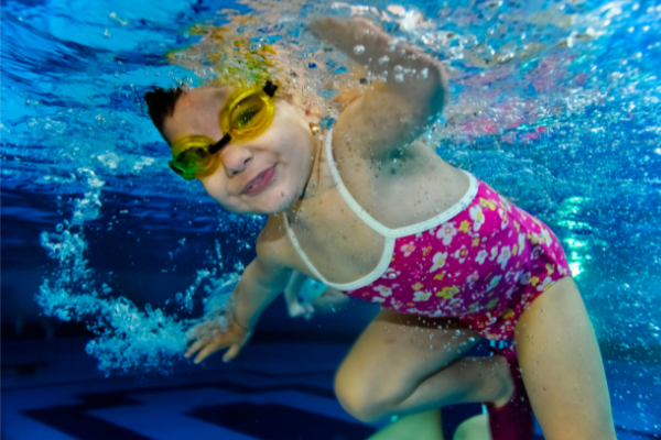 toddler swimming in pink bathing suit with yellow goggles