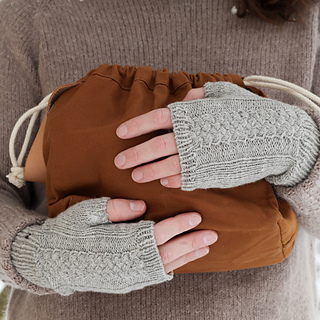 hands holding a bag and wearing modern cable knit fingerless gloves