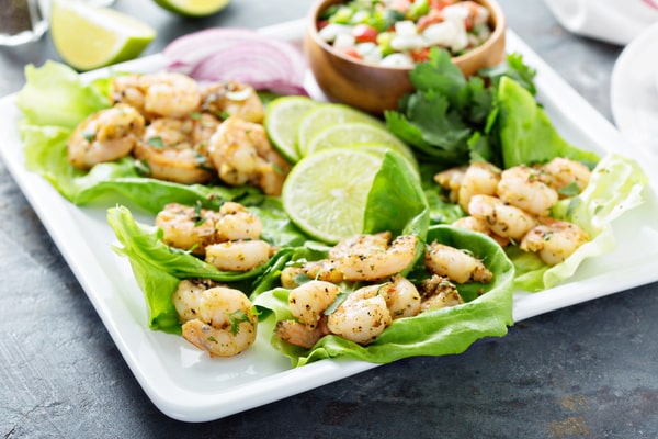 Pieces of shrimp on top of lettuce leaves with lime slices and onions on a plate
