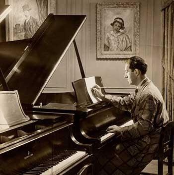 George Gershwin sits at a piano, marking sheet music.