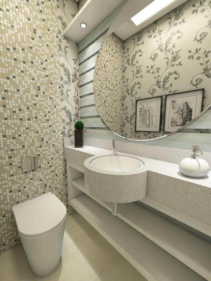 Lavabo com pia marmorizada, louças brancas, espelho redondo e pastilhas em tons neutros e parede de fundo com papel de parede floral.