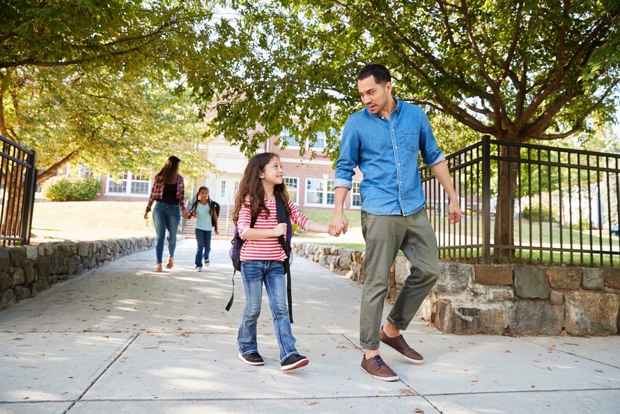 a father and daughter holding hand while walking out the gates of a school