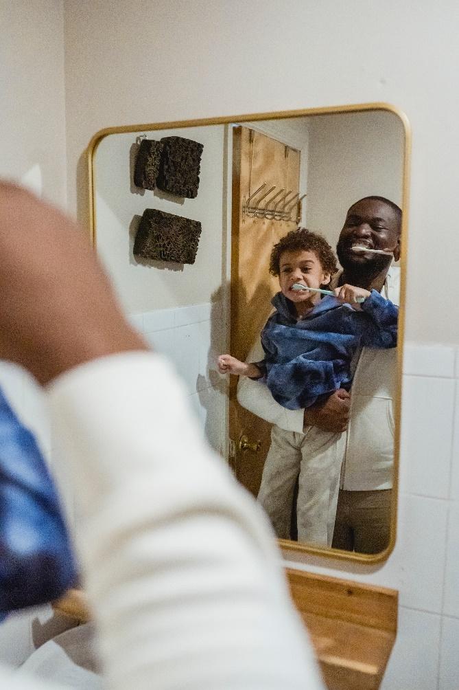 A person holding a child brushing his teeth
Description automatically generated