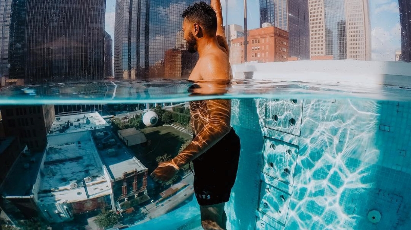 man wading in rooftop pool overlooking downtown Dallas, TX