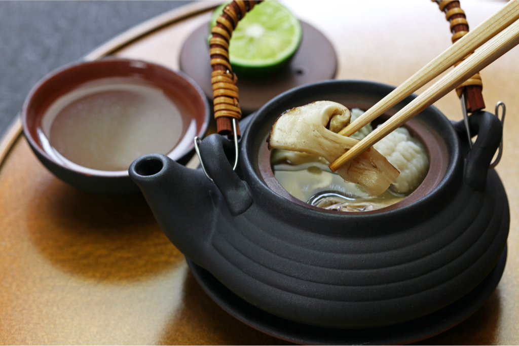 Matsutake mushroom soup in a black dobin teapot with a bowl of broth in the background is a Traditional Autumn Flavors of Japan