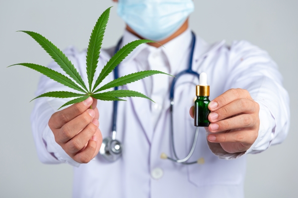 medical-doctor-holding-cannabis-leaf-bottle-cannabis-oil-white-wall