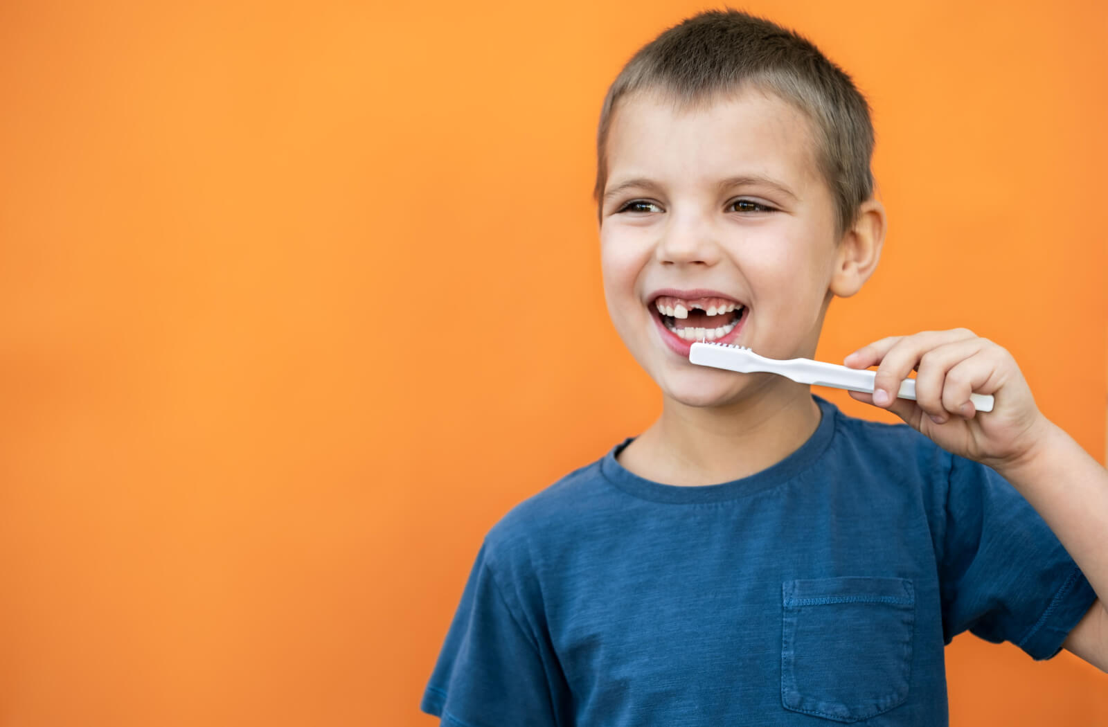 a child missing his front tooth smiles while holding a toothbrush up to his teeth
