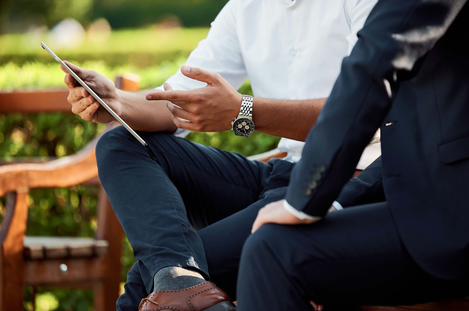 Two men and a tablet talking on a park bench.