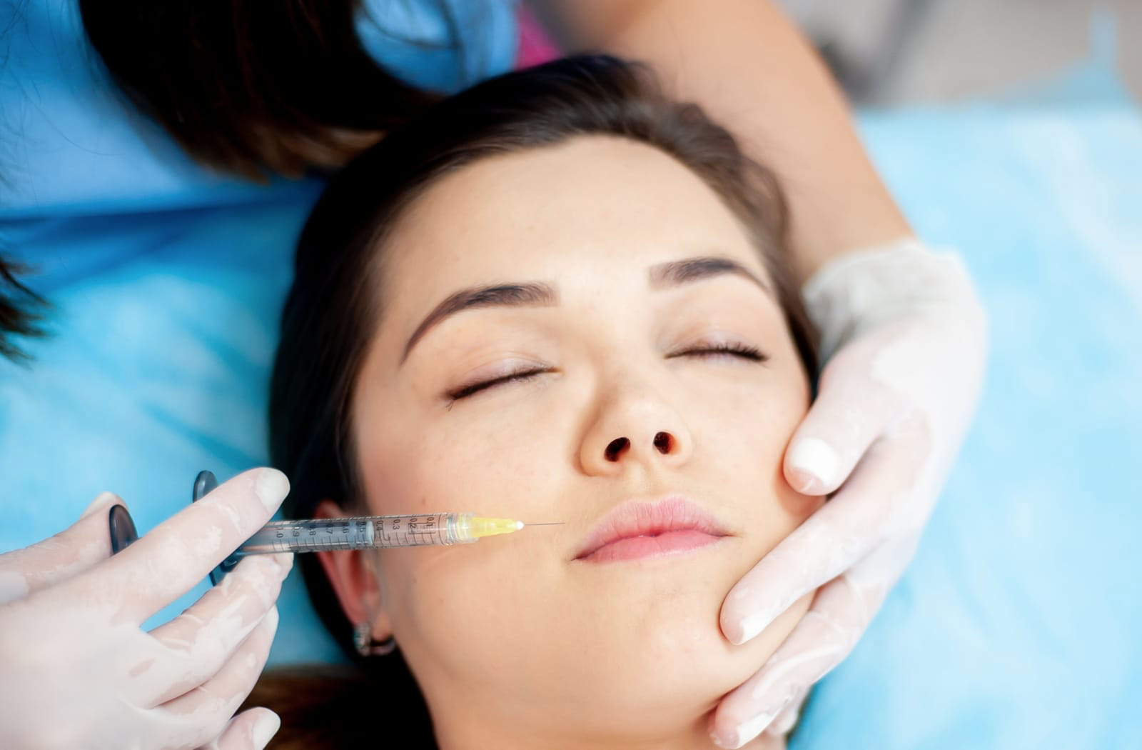 Calm woman receiving dermal fillers around her lips by gloved hands.
