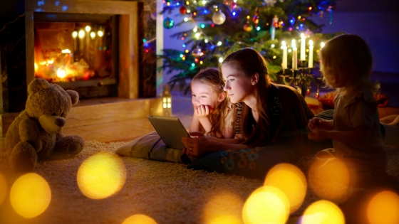 two kids watching a movie on a laptop in a room dimly lit by holiday lights. 
