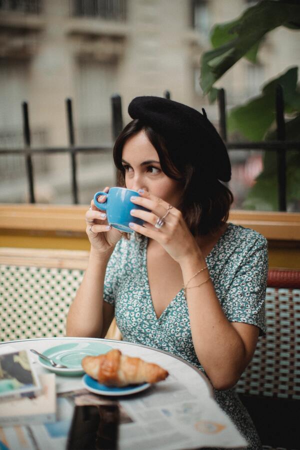 Uma mulher tomando um café em uma cafeteria e comendo um croissant de chocolate
