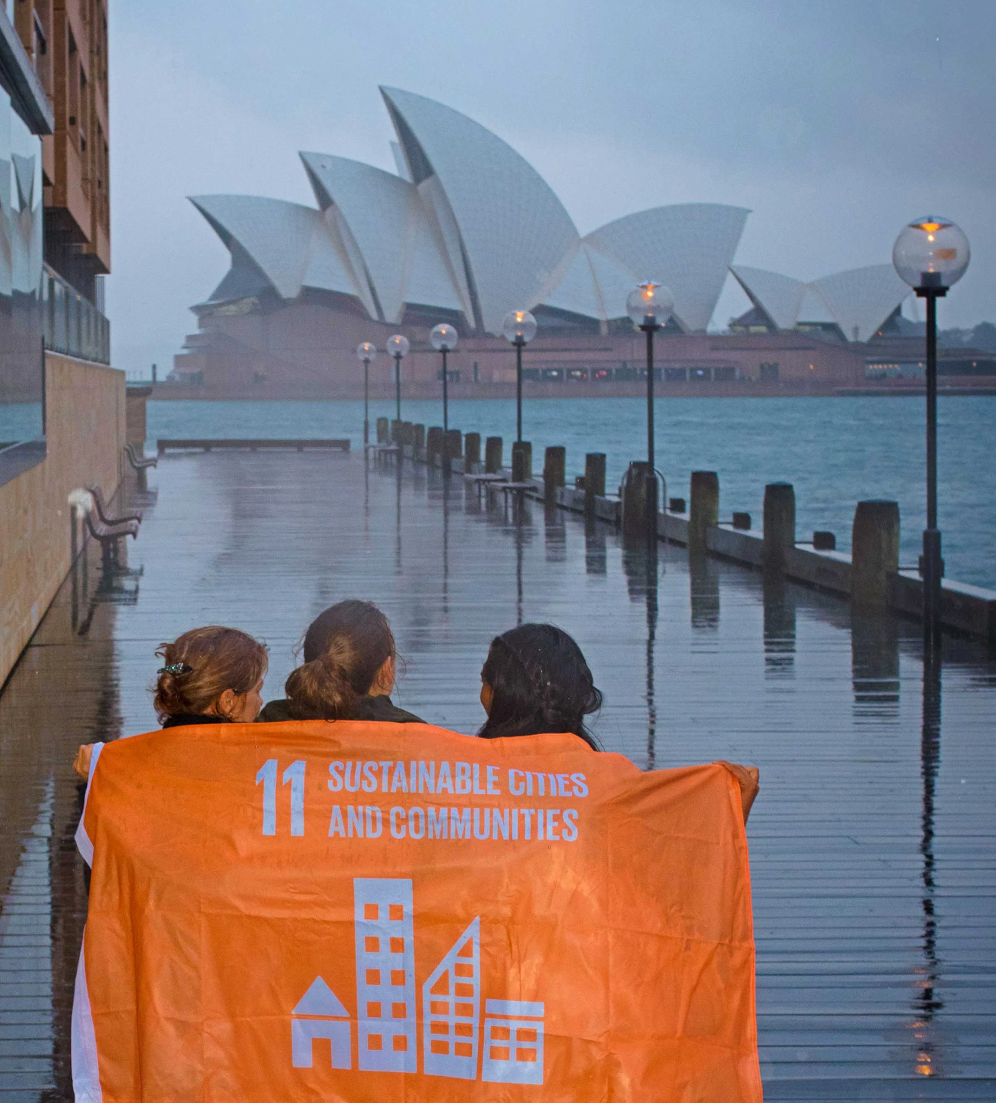 3 students holding the flag for UN's SDG 11 about sustainable cities and communities in Sydney, Australia.