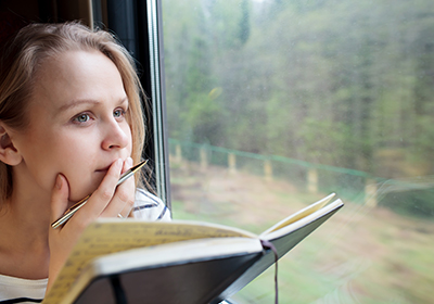 A woman in a train looking out the window while holding a pen and a journal