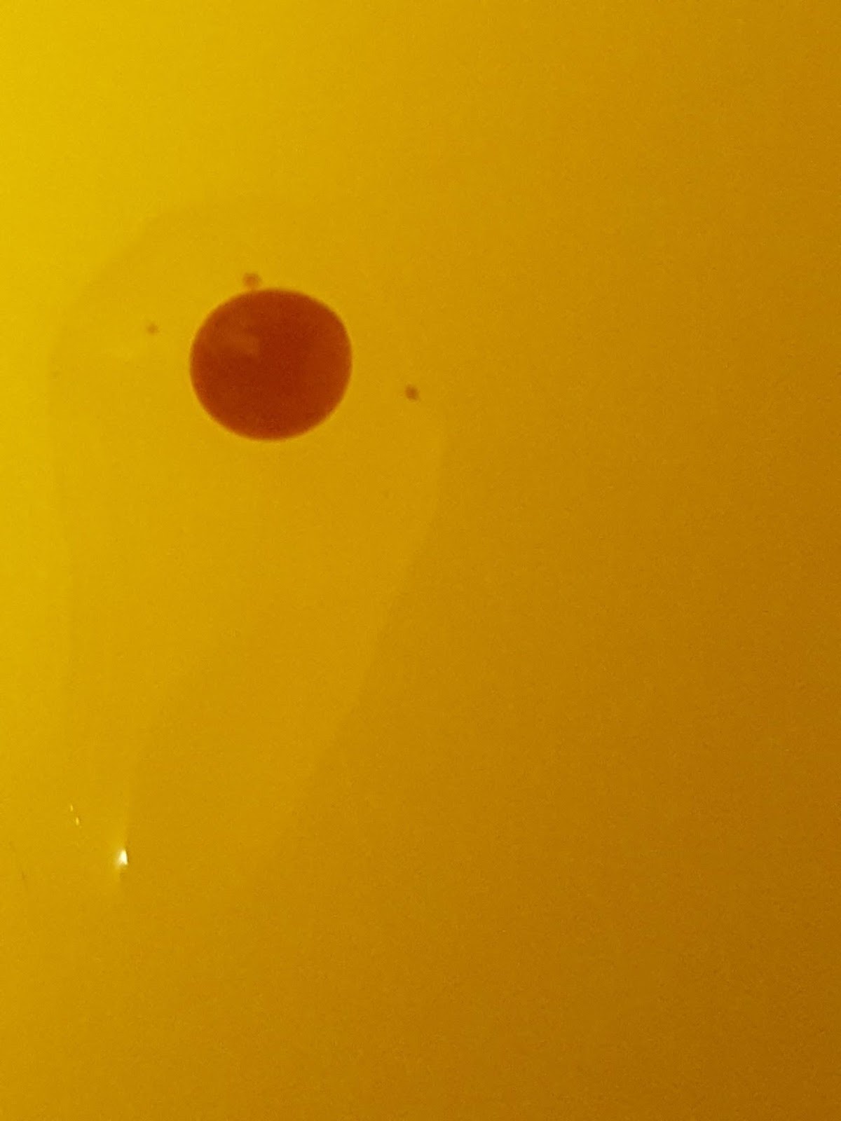 A brown drop is surrounded by a clear drop that is longer than it is wide. The background is yellow